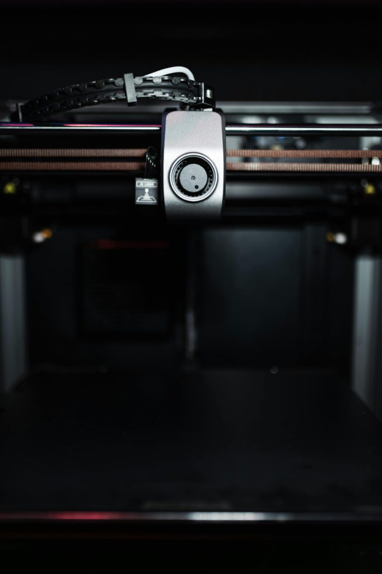 Close-up of a high-precision industrial 3D printer nozzle in a dark setting, showcasing advanced technology.
